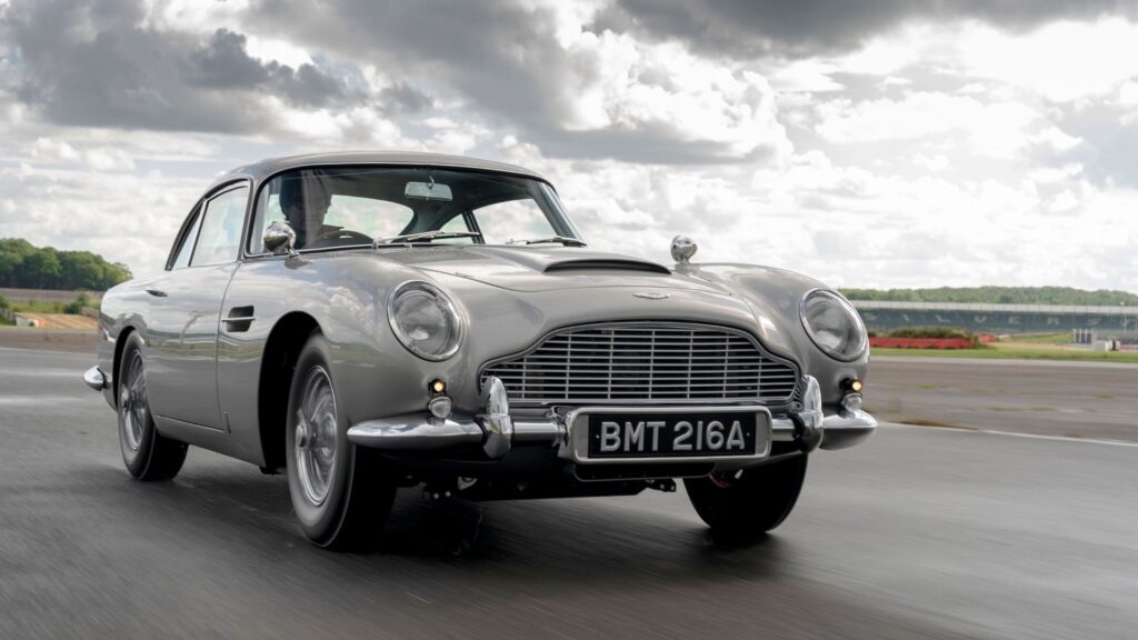 A silver car driving down the road under cloudy skies.