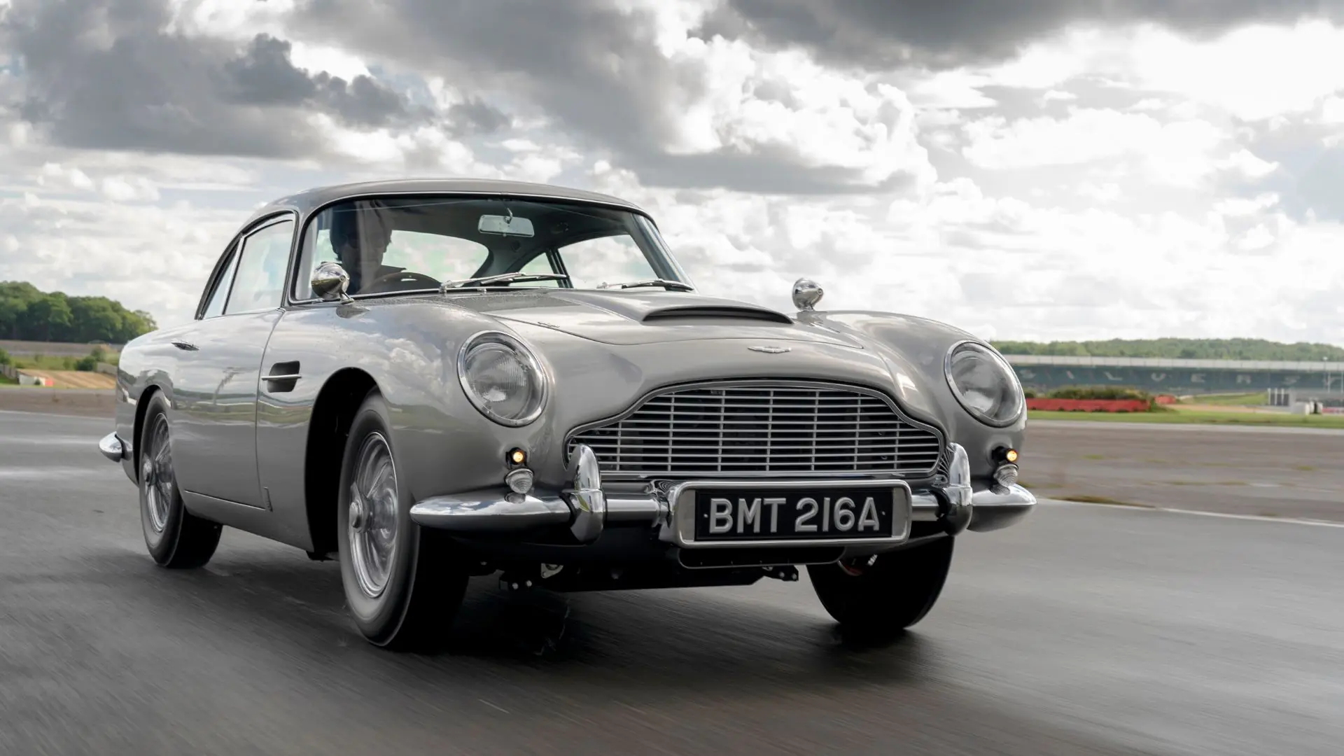 A silver car driving down the road under cloudy skies. A silver car driving down the road under cloudy skies.