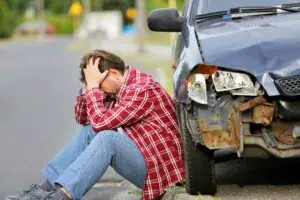 A man sitting on the ground next to a car. A man sitting on the ground next to a car.