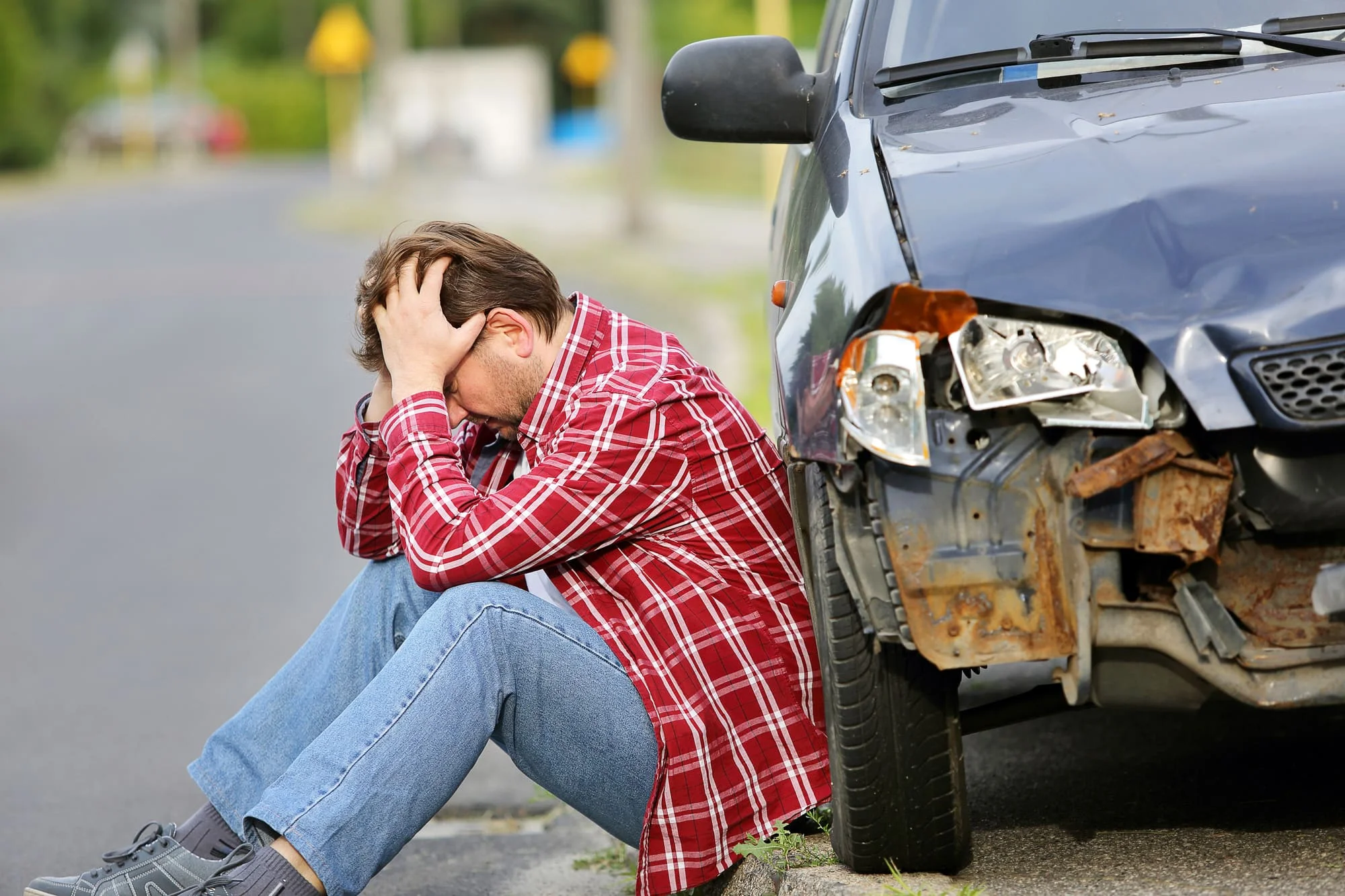 A man sitting on the ground next to a car.